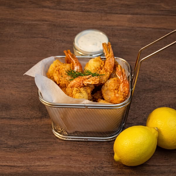 Crispy fried shrimp in a metal basket with tartar sauce, fresh lemons, and dill garnish.