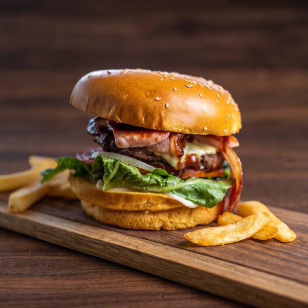 A gourmet bacon cheeseburger with lettuce, onion, and sauce, served with fries on a wooden board.