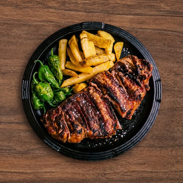 Sliced grilled meat, french fries, and green peppers on a black plate, sprinkled with salt.