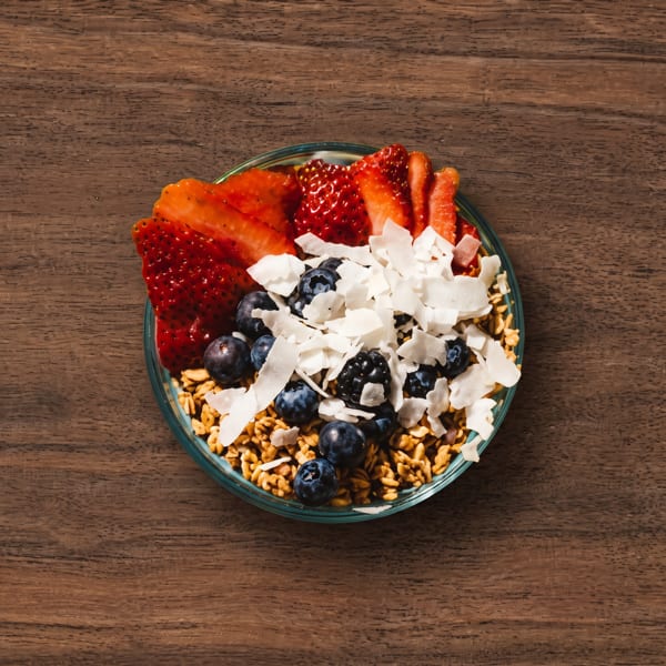 Granola bowl topped with sliced strawberries, blueberries, and coconut flakes on a wooden table.